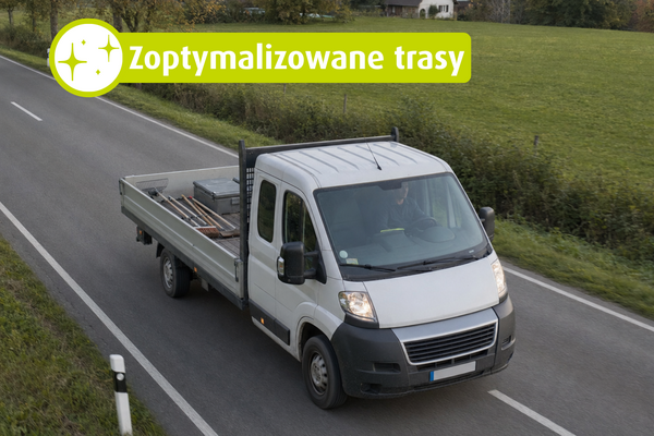 Biała ciężarówka z otwartą platformą jedzie wiejską drogą. Tekst na obrazie: „Zoptymalizowane trasy“.