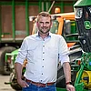 Mitarbeiter der Quathamer GmbH steht vor grünem Traktor im landwirtschaftlichen Betrieb